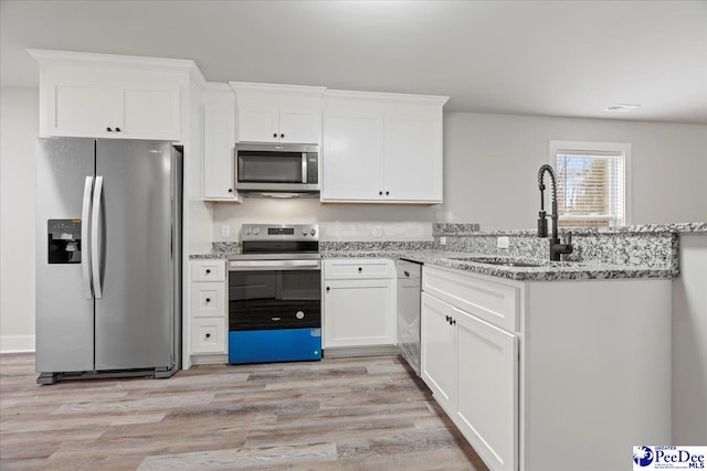 kitchen featuring appliances with stainless steel finishes, sink, white cabinets, light stone counters, and light hardwood / wood-style floors