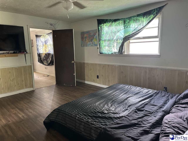 bedroom with wooden walls, ceiling fan, dark hardwood / wood-style floors, and a textured ceiling