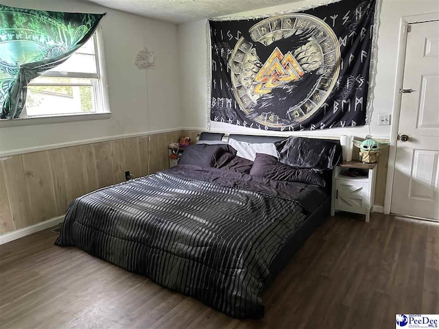 bedroom with wooden walls, a textured ceiling, and dark hardwood / wood-style flooring