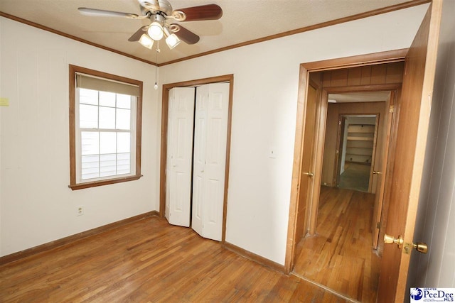 unfurnished bedroom with hardwood / wood-style flooring, ornamental molding, a closet, and ceiling fan