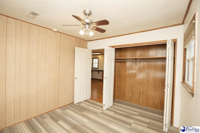 unfurnished bedroom featuring ceiling fan, crown molding, wooden walls, and a closet