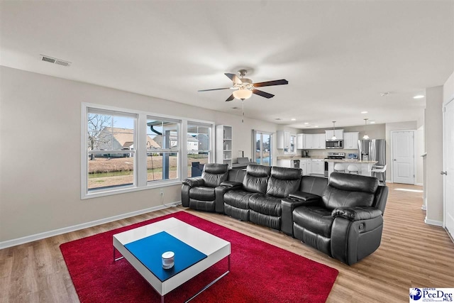 living area with a ceiling fan, light wood-type flooring, visible vents, and baseboards