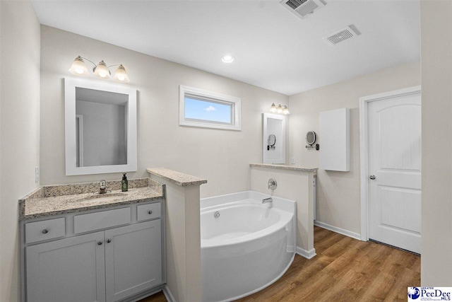 bathroom featuring a garden tub, visible vents, wood finished floors, and vanity