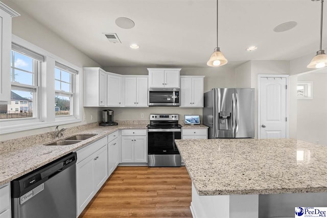 kitchen with appliances with stainless steel finishes, pendant lighting, white cabinets, and a sink