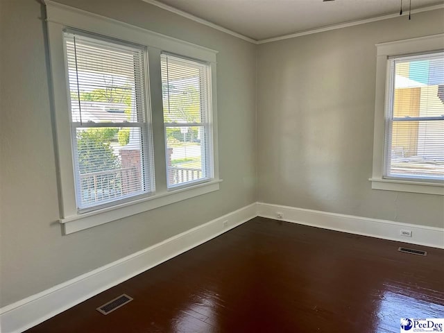 empty room featuring dark wood-type flooring, visible vents, baseboards, and crown molding