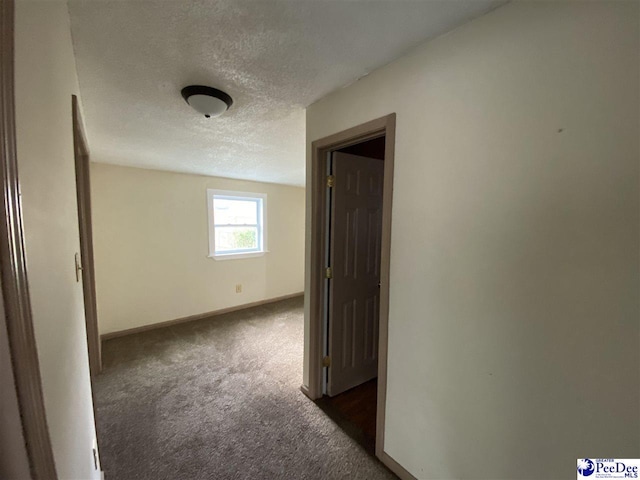 spare room featuring baseboards, dark colored carpet, and a textured ceiling