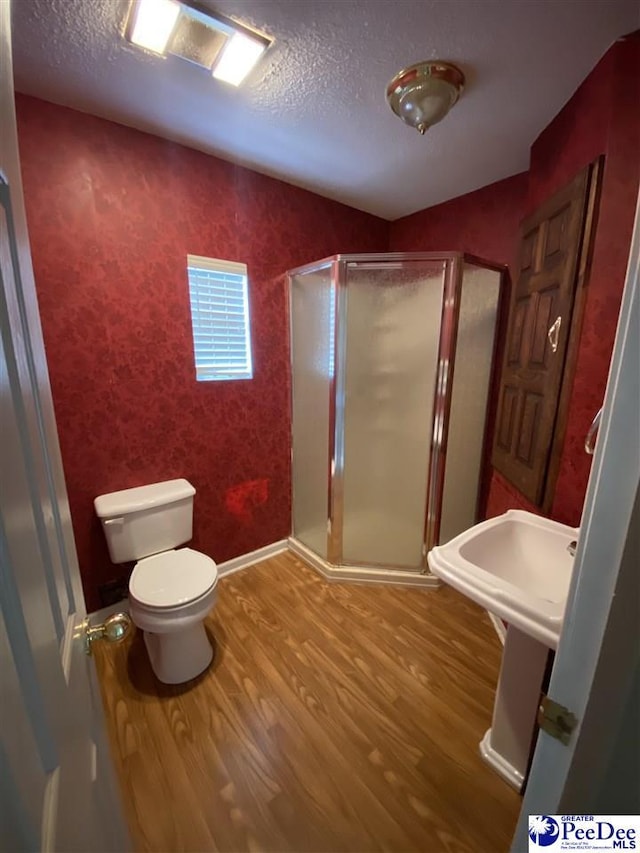 full bath featuring a textured ceiling, wood finished floors, toilet, and a shower stall