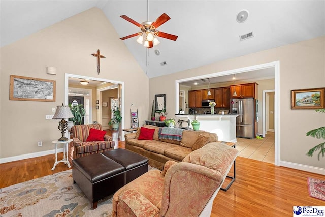 living area featuring high vaulted ceiling, visible vents, baseboards, a ceiling fan, and light wood finished floors