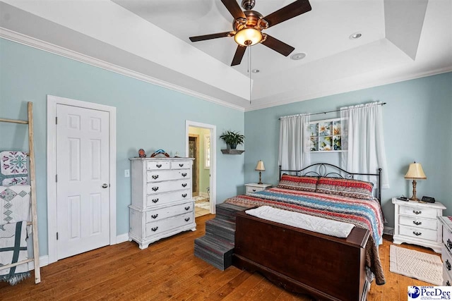 bedroom with crown molding, a tray ceiling, connected bathroom, and wood finished floors