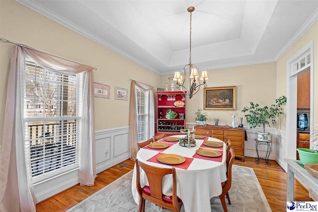 dining room with a wainscoted wall, a tray ceiling, a chandelier, and light wood-style floors