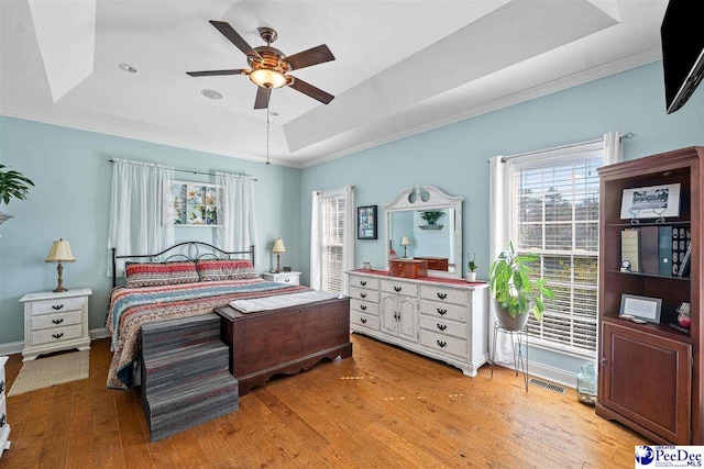 bedroom with baseboards, visible vents, a raised ceiling, crown molding, and light wood-style floors