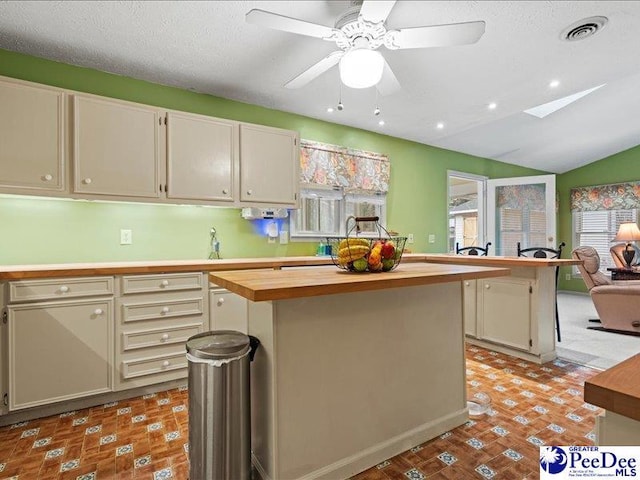 kitchen with butcher block countertops, ceiling fan, lofted ceiling with skylight, a center island, and a textured ceiling