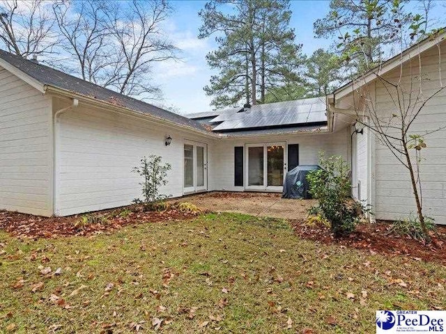 rear view of house featuring a yard and solar panels