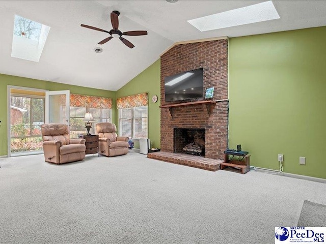 living room featuring a skylight, high vaulted ceiling, a brick fireplace, ceiling fan, and carpet