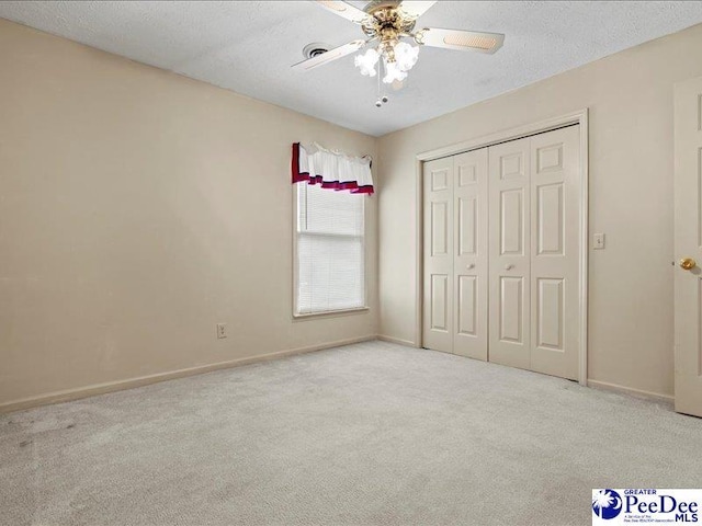 unfurnished bedroom featuring ceiling fan, light colored carpet, a textured ceiling, and a closet