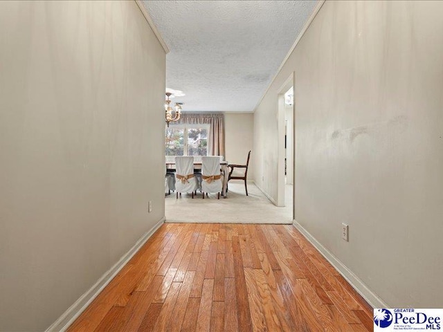 corridor with a notable chandelier, a textured ceiling, and light wood-type flooring