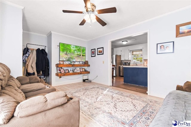 living area featuring baseboards, light wood-style flooring, a ceiling fan, and crown molding