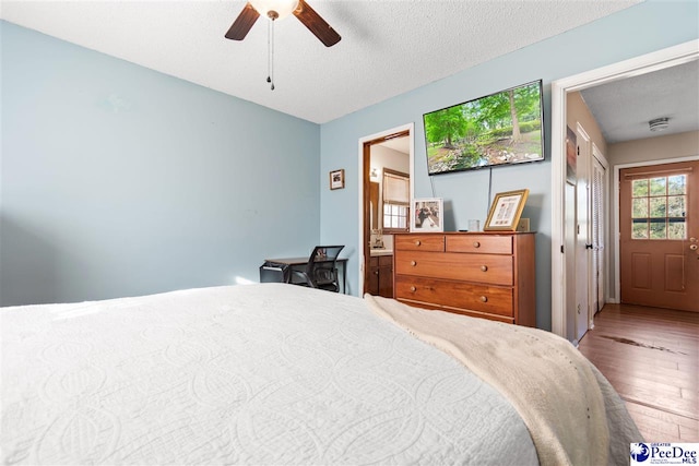 bedroom with ceiling fan, connected bathroom, a textured ceiling, and wood finished floors