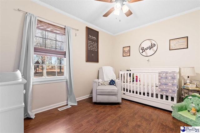 bedroom with a nursery area, wood finished floors, visible vents, and crown molding