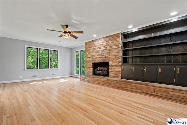 unfurnished living room with built in features, ceiling fan, ornamental molding, light hardwood / wood-style floors, and a stone fireplace