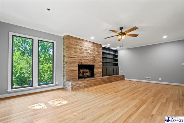 unfurnished living room with crown molding, light hardwood / wood-style flooring, ceiling fan, a fireplace, and built in shelves