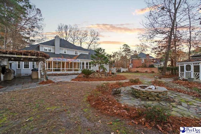 3406 Sussex Ct, Florence, SC 29501 - back house at dusk with an outdoor fire pit, a patio area, and a sunroom
