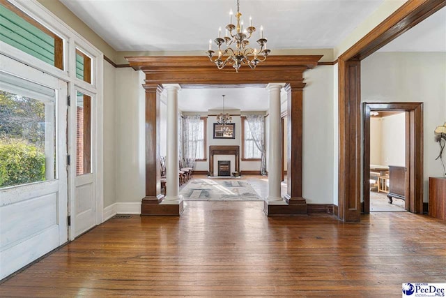 foyer with an inviting chandelier, dark wood-type flooring, and decorative columns