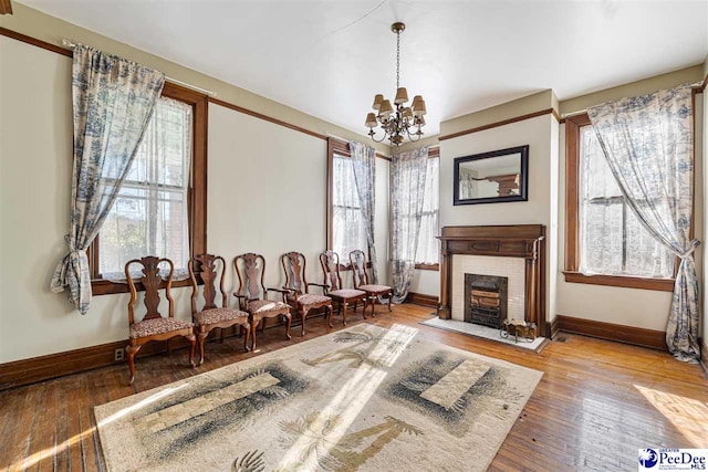 sitting room featuring a notable chandelier, wood-type flooring, a healthy amount of sunlight, and a brick fireplace