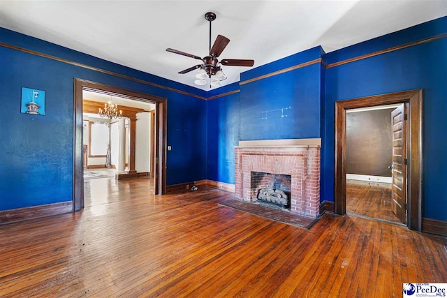 unfurnished living room with a brick fireplace, ceiling fan with notable chandelier, and dark hardwood / wood-style floors