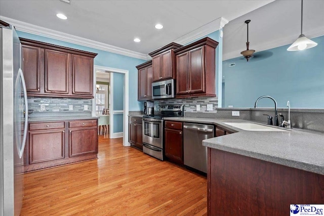 kitchen featuring light wood-style flooring, a sink, decorative light fixtures, appliances with stainless steel finishes, and crown molding