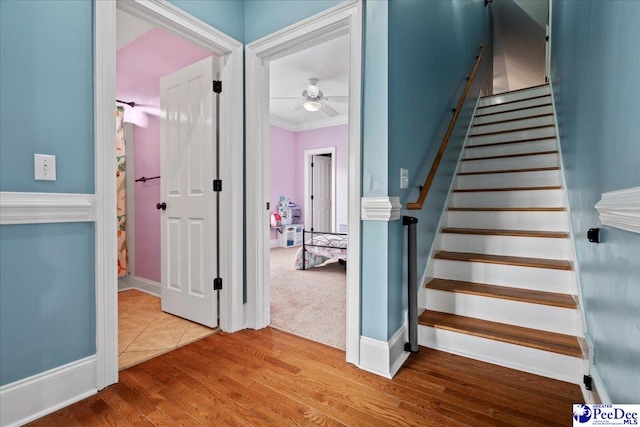 stairway with a ceiling fan, wood finished floors, and ornamental molding