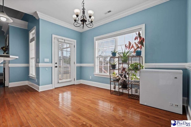 entryway featuring baseboards, visible vents, ornamental molding, hardwood / wood-style flooring, and a chandelier