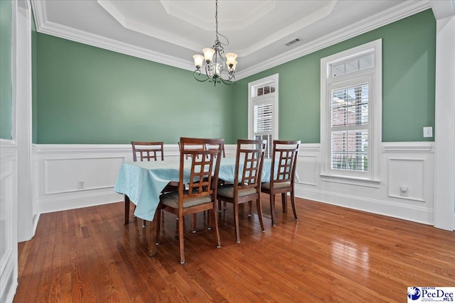 dining room with visible vents, a chandelier, a wainscoted wall, wood finished floors, and a raised ceiling