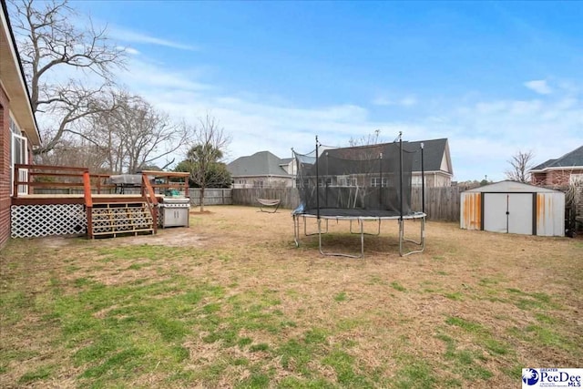 view of yard with an outbuilding, a trampoline, a fenced backyard, a shed, and a wooden deck