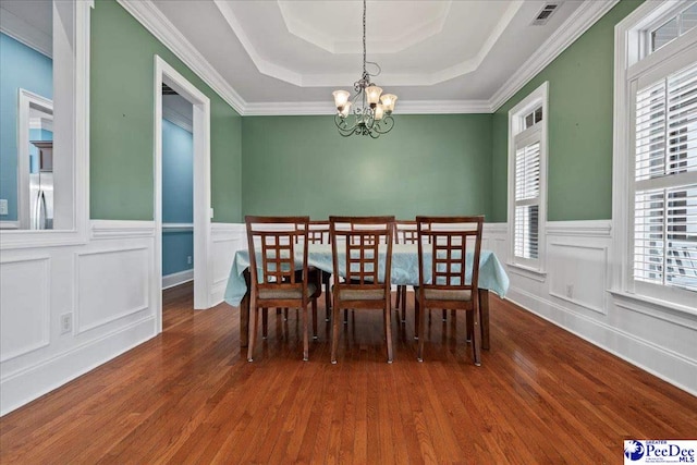 dining room featuring a chandelier, visible vents, a tray ceiling, and wood finished floors