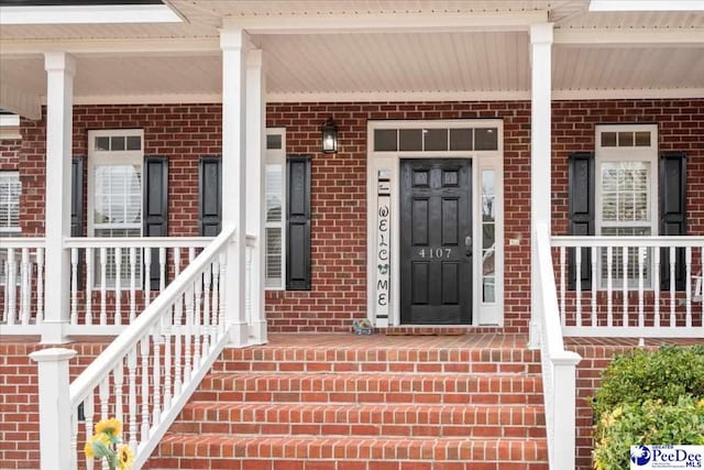 doorway to property with a porch and brick siding