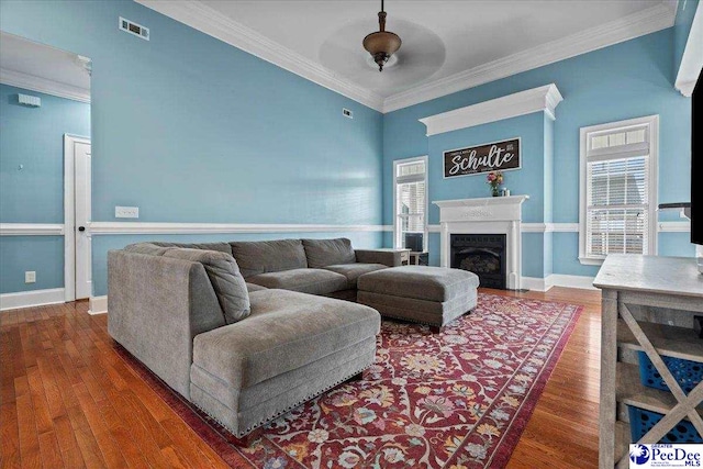 living area featuring a fireplace, crown molding, wood finished floors, and visible vents