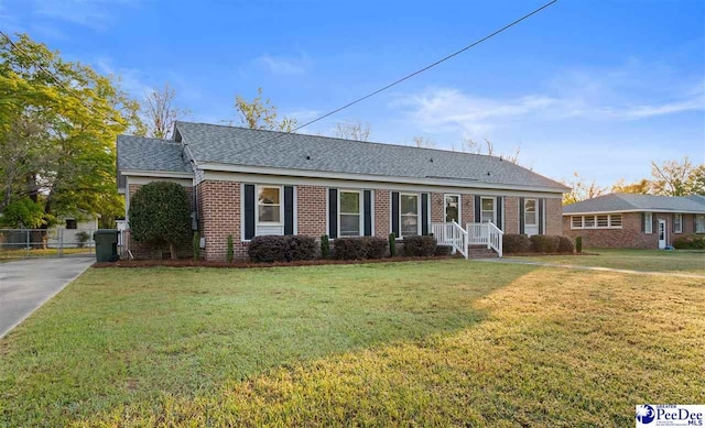 ranch-style home featuring a shingled roof, fence, a front lawn, and brick siding