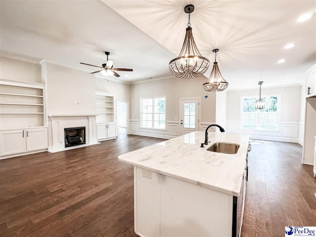 kitchen with pendant lighting, sink, light stone counters, and a center island with sink