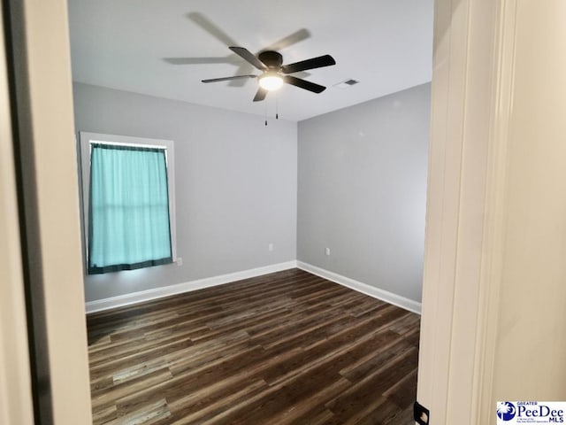 spare room featuring visible vents, a ceiling fan, dark wood-type flooring, and baseboards