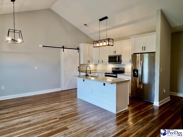 kitchen with a center island with sink, appliances with stainless steel finishes, white cabinetry, and a barn door