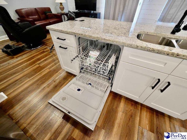 kitchen with a sink, light stone counters, dark wood-style floors, and white cabinetry