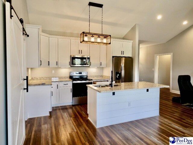 kitchen with a center island with sink, a sink, white cabinets, appliances with stainless steel finishes, and a barn door