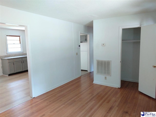 unfurnished bedroom with a closet, a spacious closet, light hardwood / wood-style floors, and white fridge