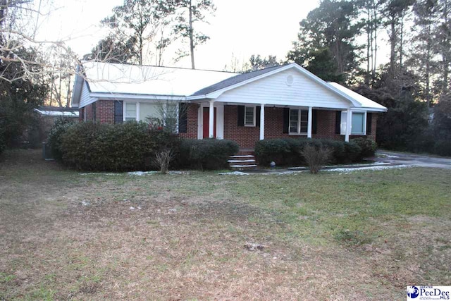 ranch-style home featuring covered porch, brick siding, and a front lawn