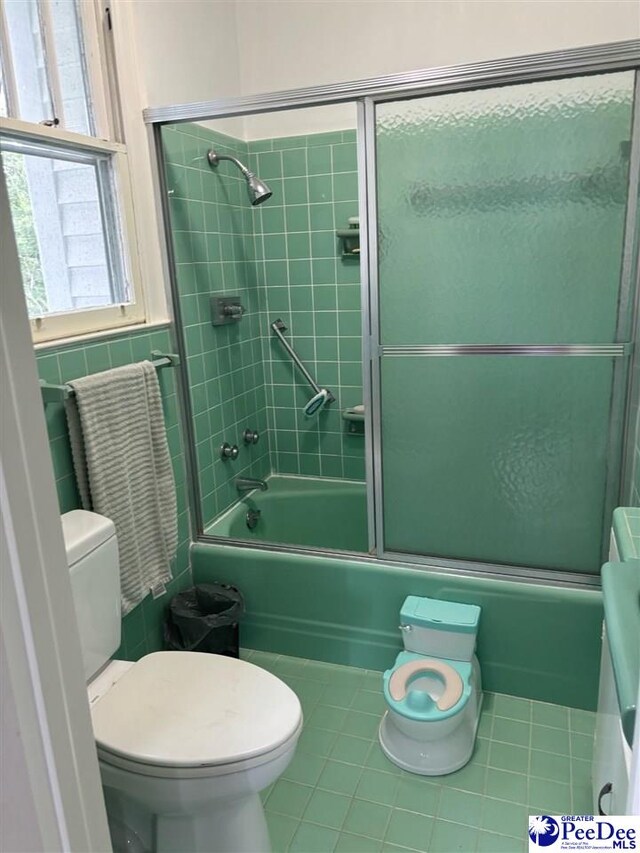 bathroom with tile patterned floors, toilet, combined bath / shower with glass door, and tile walls