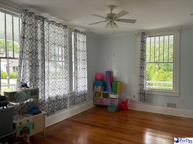 recreation room featuring hardwood / wood-style flooring, ornamental molding, and ceiling fan