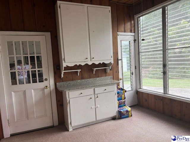 kitchen with white cabinetry, light carpet, and wooden walls