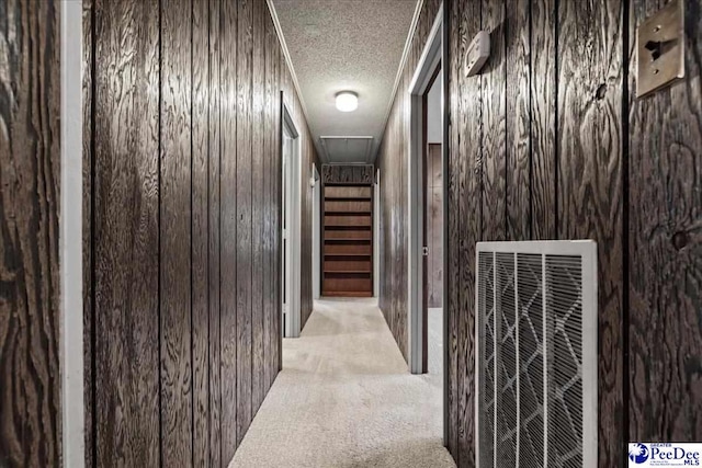 corridor with light colored carpet, a textured ceiling, and wood walls