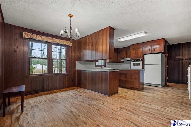 kitchen with wood walls, decorative light fixtures, light wood-type flooring, a notable chandelier, and white appliances